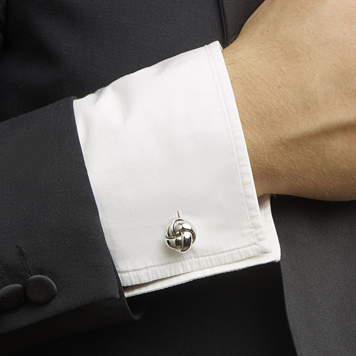 Close-up van de pols van een persoon met een witte overhemdmanchet en een zilveren manchetknoop in de vorm van een knoop.