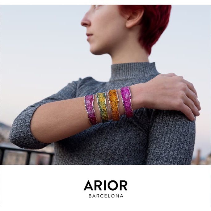 Vrouw draagt kleurrijke glinsterende armbanden, grijs topje. Logo