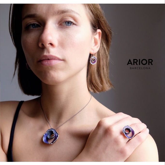 Vrouw draagt blauwe en zilveren sieraden: ketting, oorbellen en ring.
