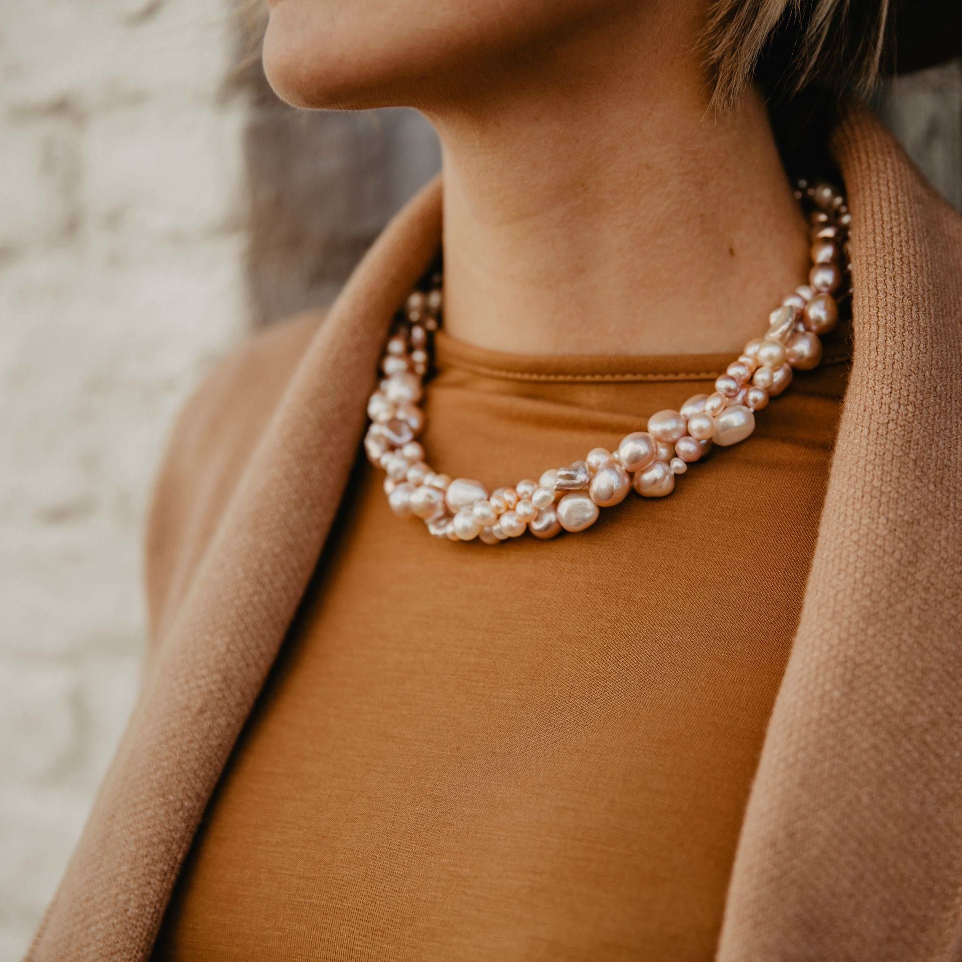 Vrouw draagt een parelketting met meerdere rijen, over een bruin topje en een bruine jas.