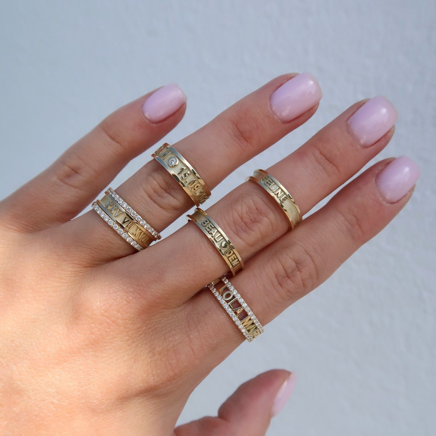 Een hand toont zes gouden ringen, waarvan sommige met diamanten, tegen een lichte achtergrond.
