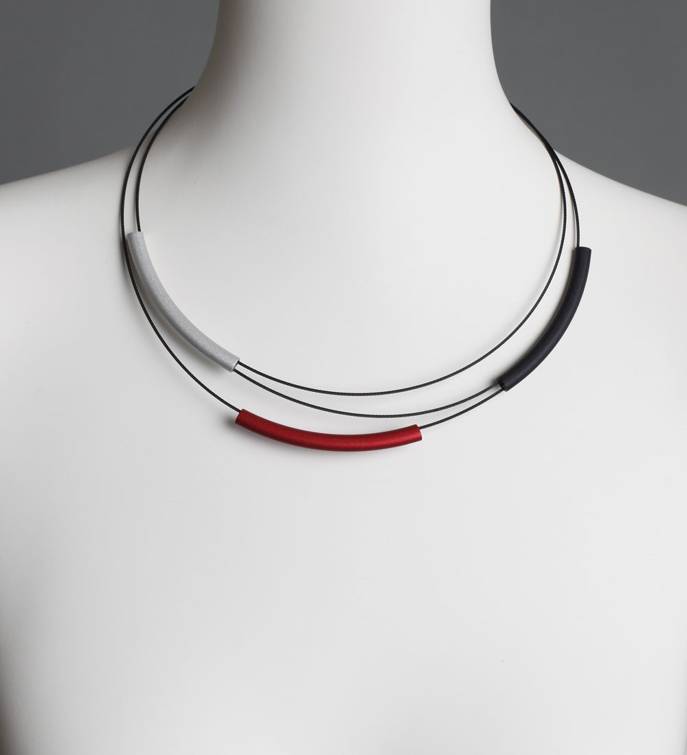 Ketting met zilveren, rode, grijze en zwarte buisjes op een mannequin.