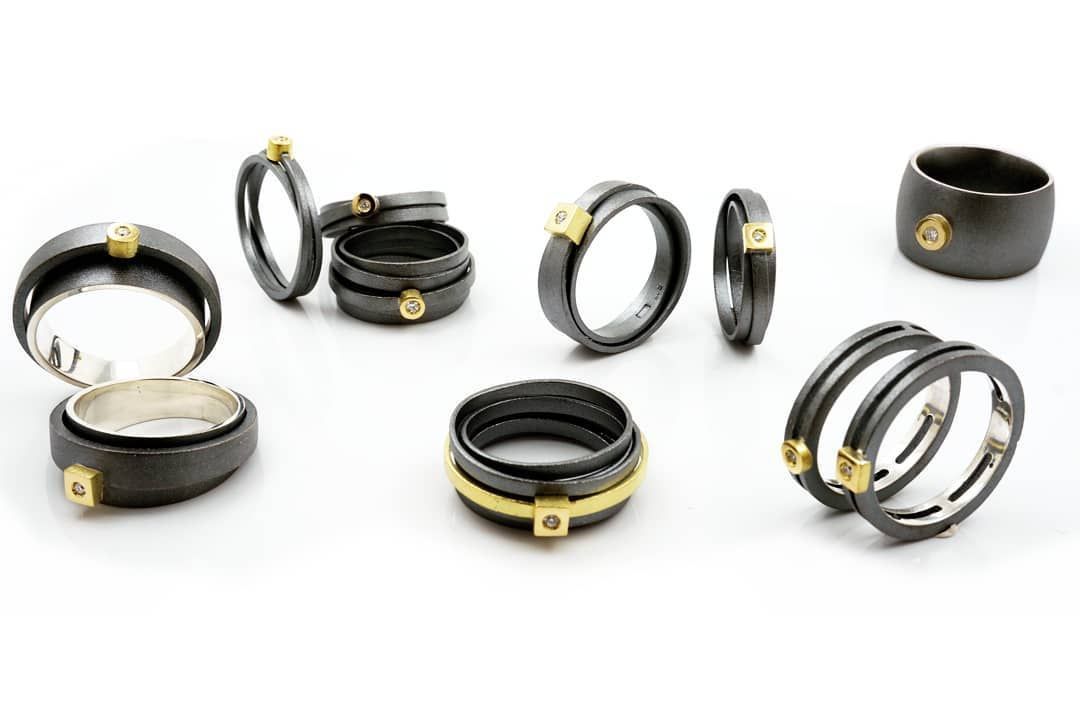 Verschillende donkere metalen ringen met gouden accenten en kleine edelstenen op een witte achtergrond.