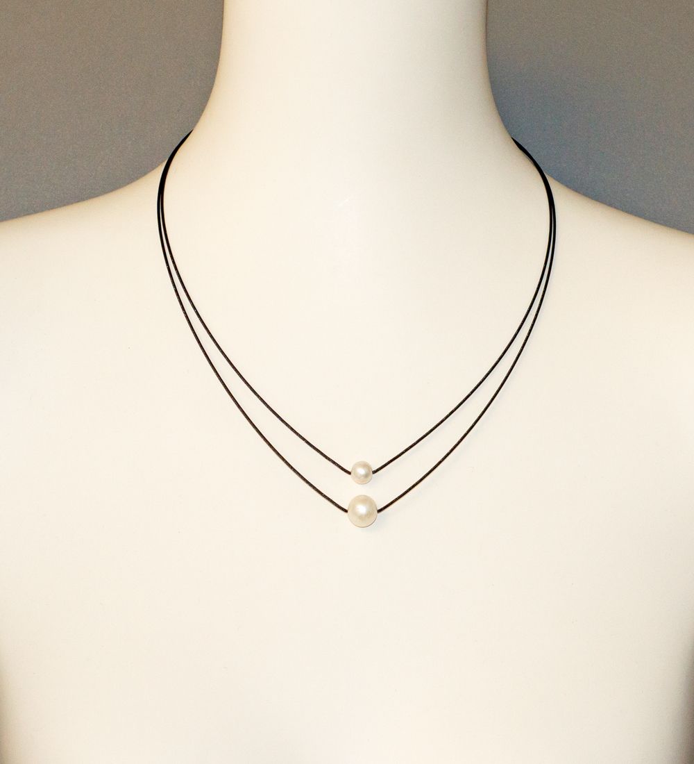 Twee-strengs ketting met parels op de nek van een mannequin. Zwarte koorden en witte parels.