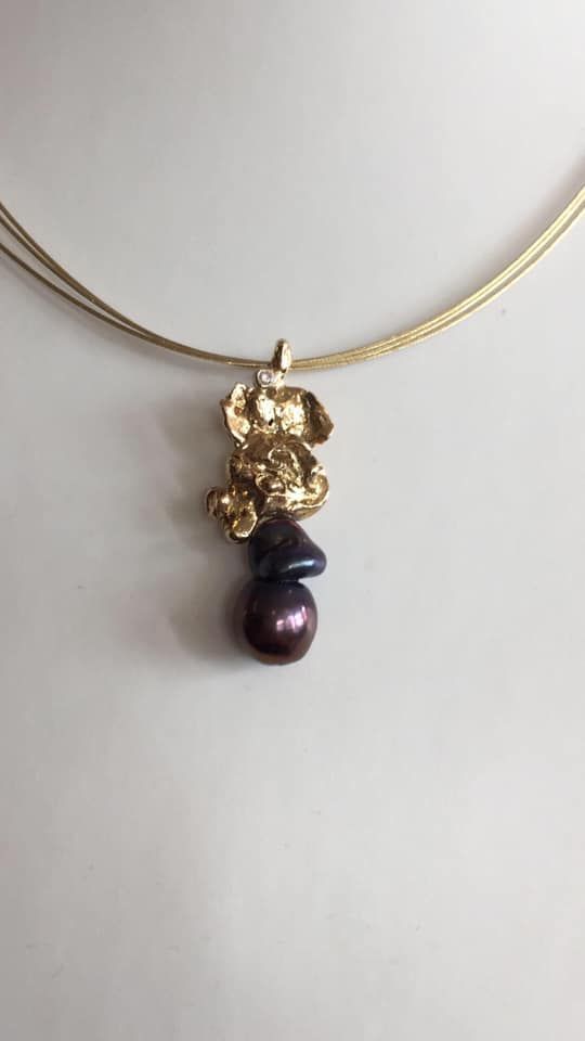 Gouden hangerketting met een cluster van goud, een donkerblauwe edelsteen en een donkere parel.