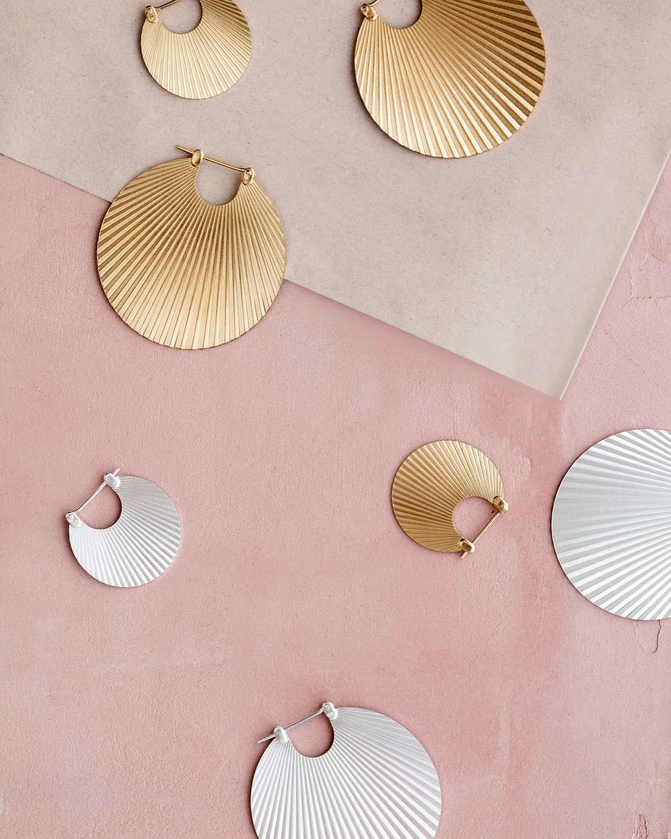 Goud- en zilverkleurige creolen met textuur op een roze en beige achtergrond.