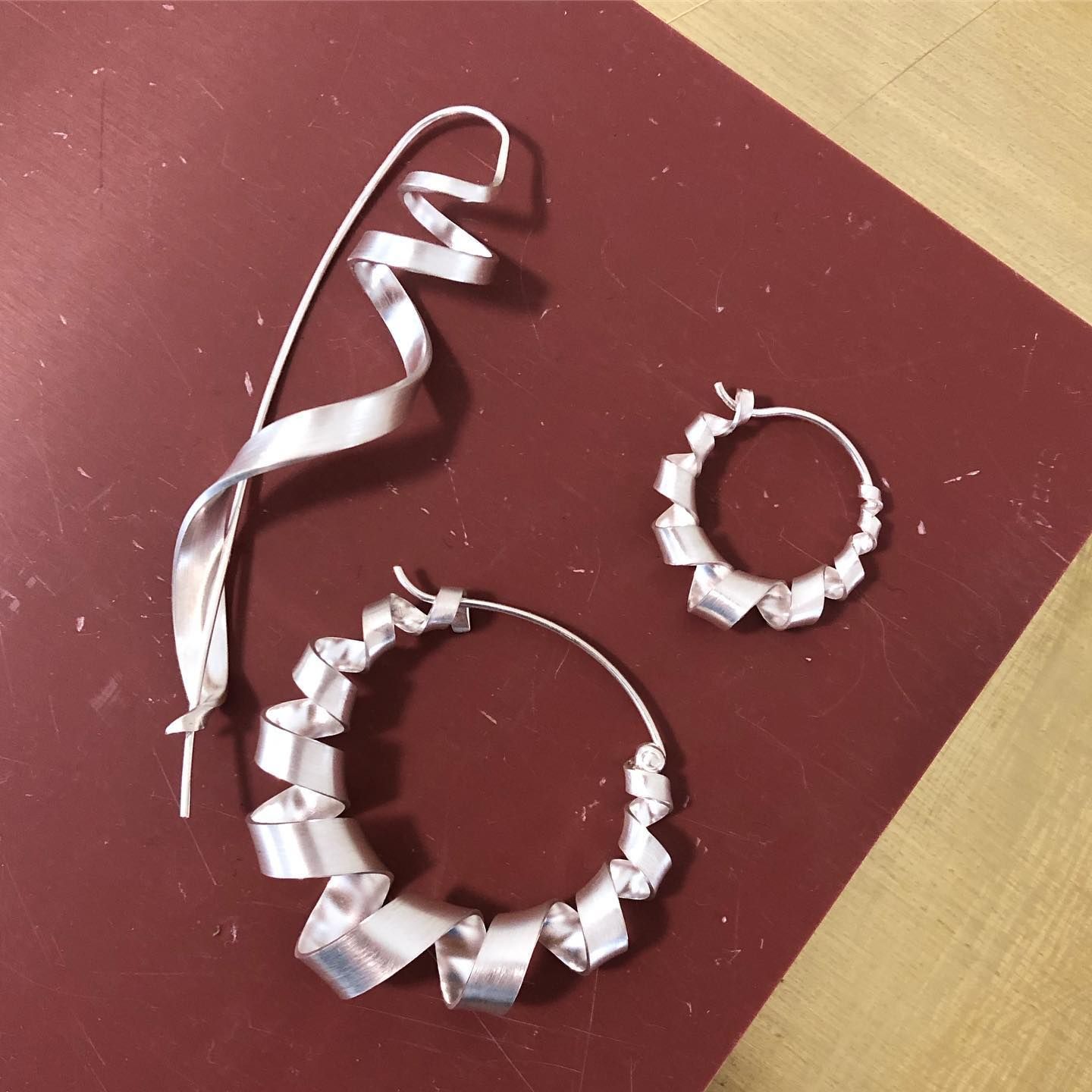 Drie zilveren oorbellen met een kastanjebruine afwerking. Eén heeft een lang, wervelend ontwerp en de twee zijn ringen met gevouwen metaal.