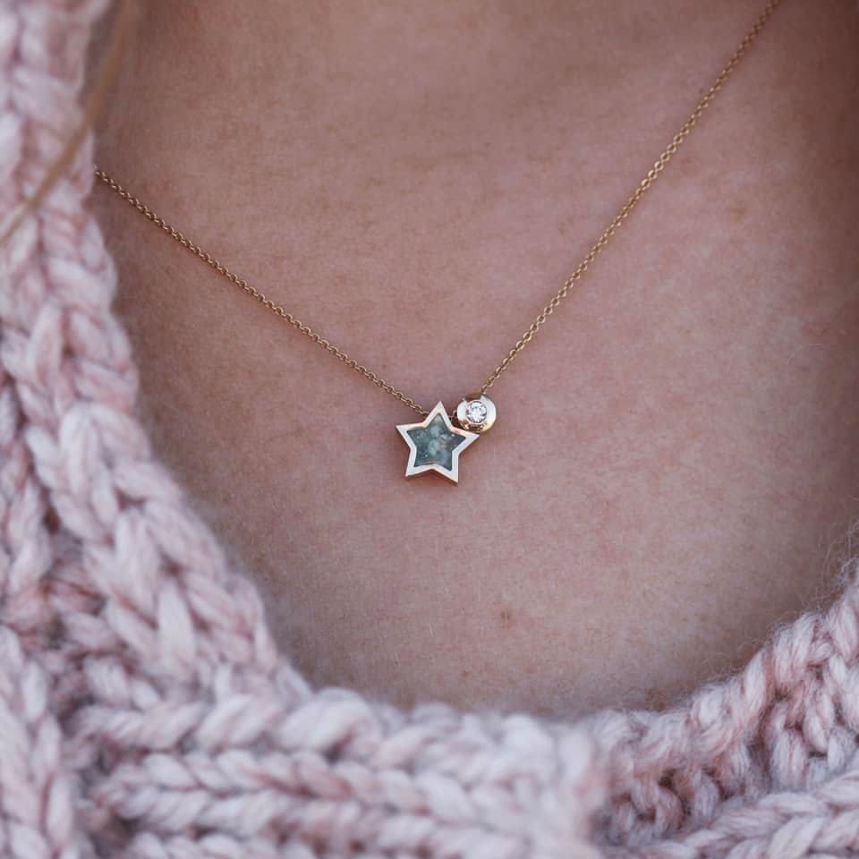 Gouden ketting met stervormige hanger, accent met diamant, rustend op een roze trui.