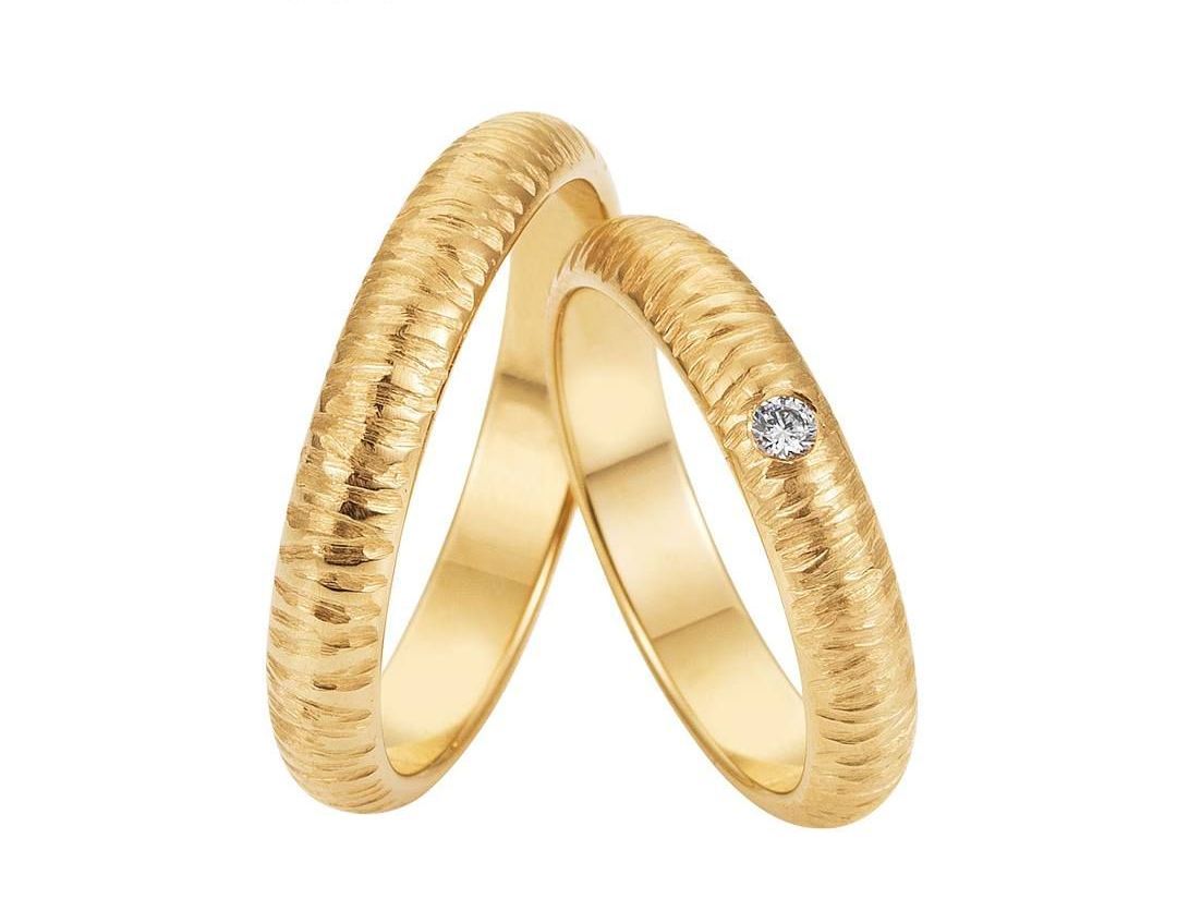 Twee gouden trouwringen, waarvan één met een klein diamantje en een gestructureerd oppervlak.