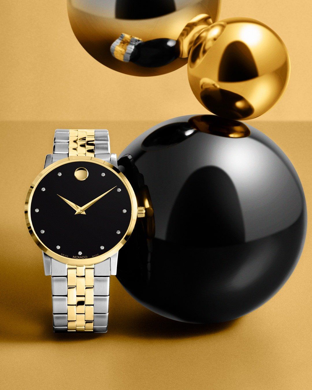 Horloge van goud en zilver met een zwarte wijzerplaat, naast een zwarte bol en gouden bollen op een gouden achtergrond.