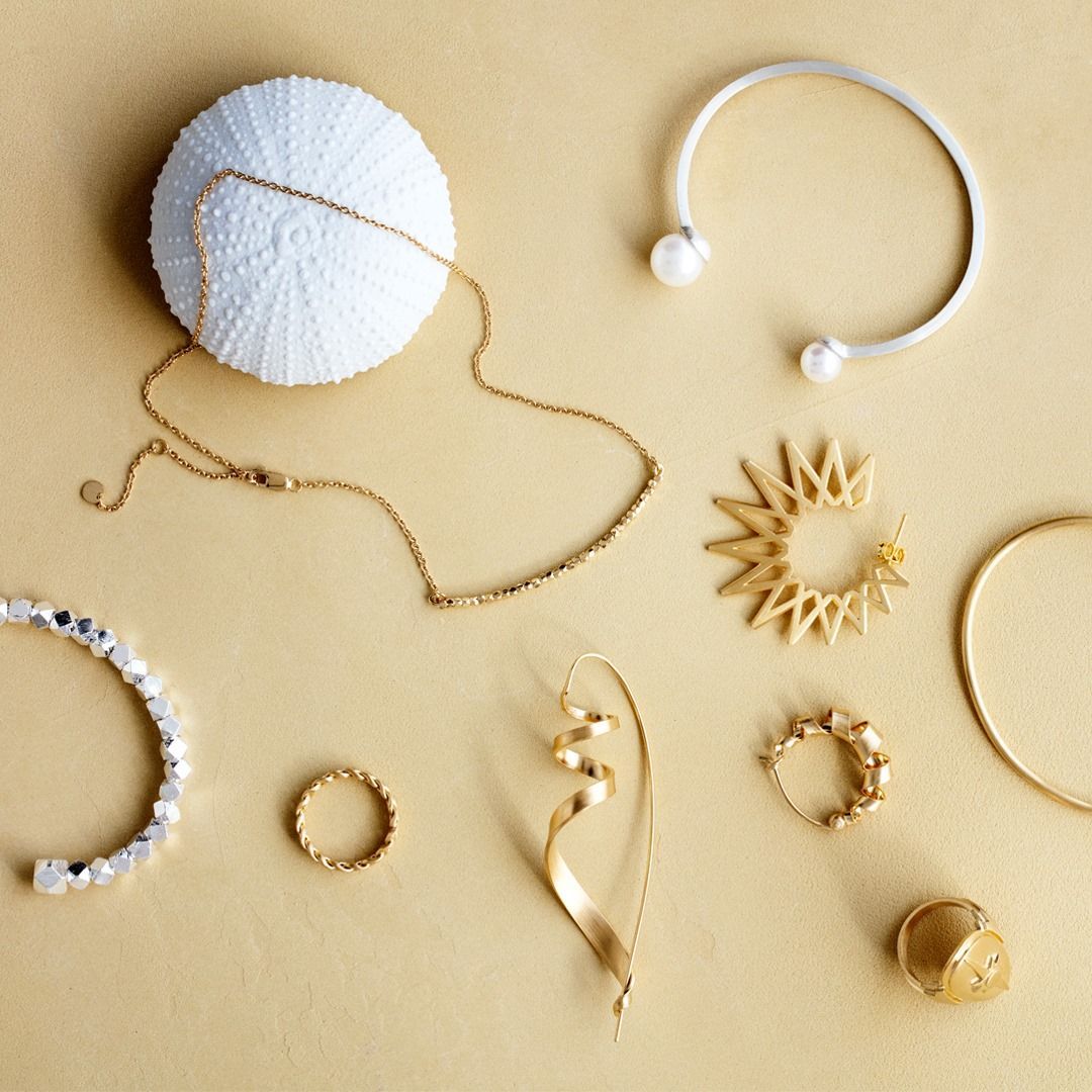 Sieradenassortiment op een gouden ondergrond: kettingen, armbanden, ringen, oorbellen, zee-egelschelpen.