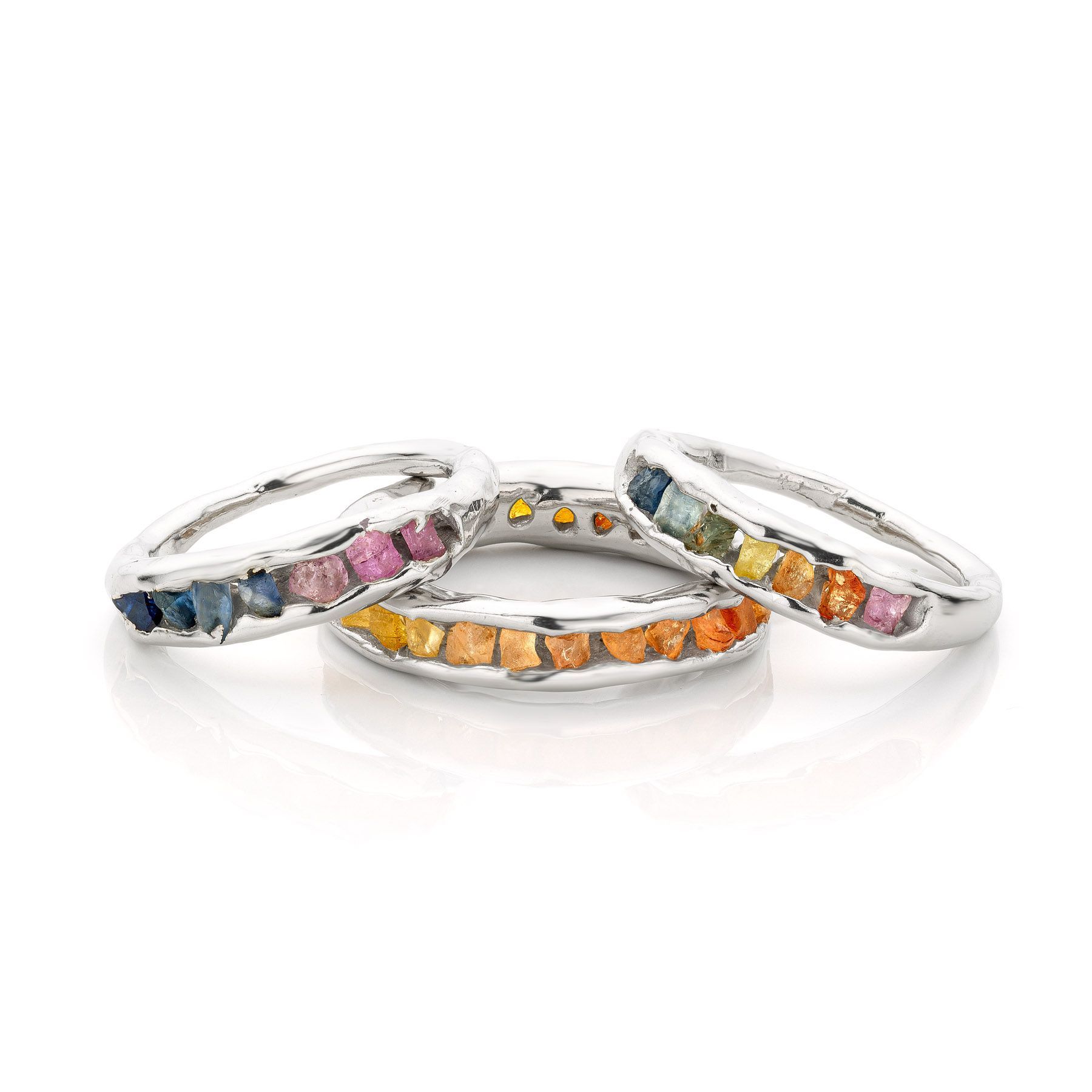 Drie zilveren ringen met een rij kleurrijke edelstenen.