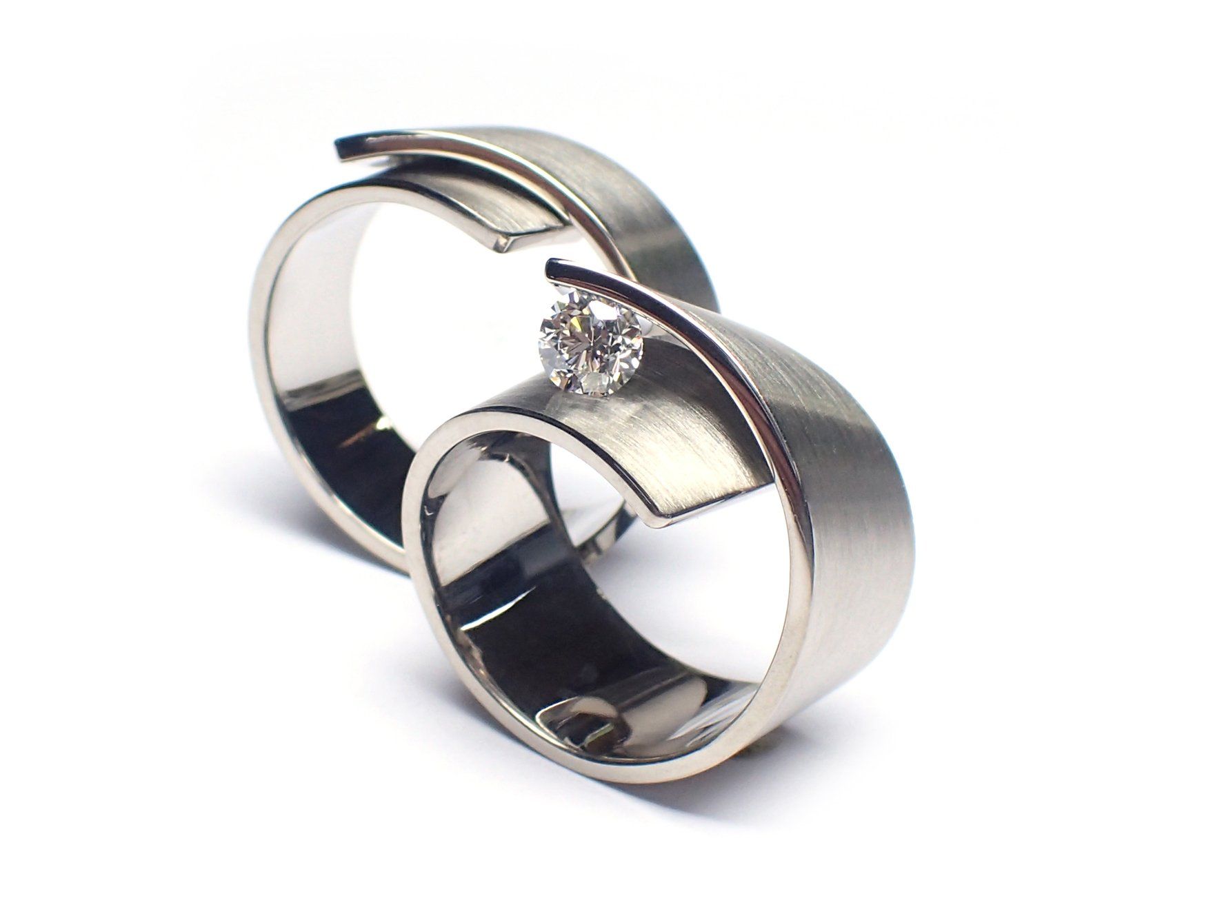 Twee moderne zilveren ringen, waarvan één met een diamant, op een witte achtergrond.