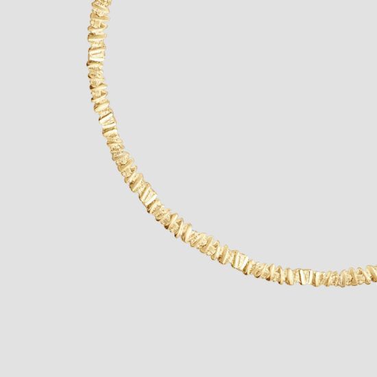 Gouden ketting, gebogen, gestructureerd oppervlak, tegen een grijze achtergrond.