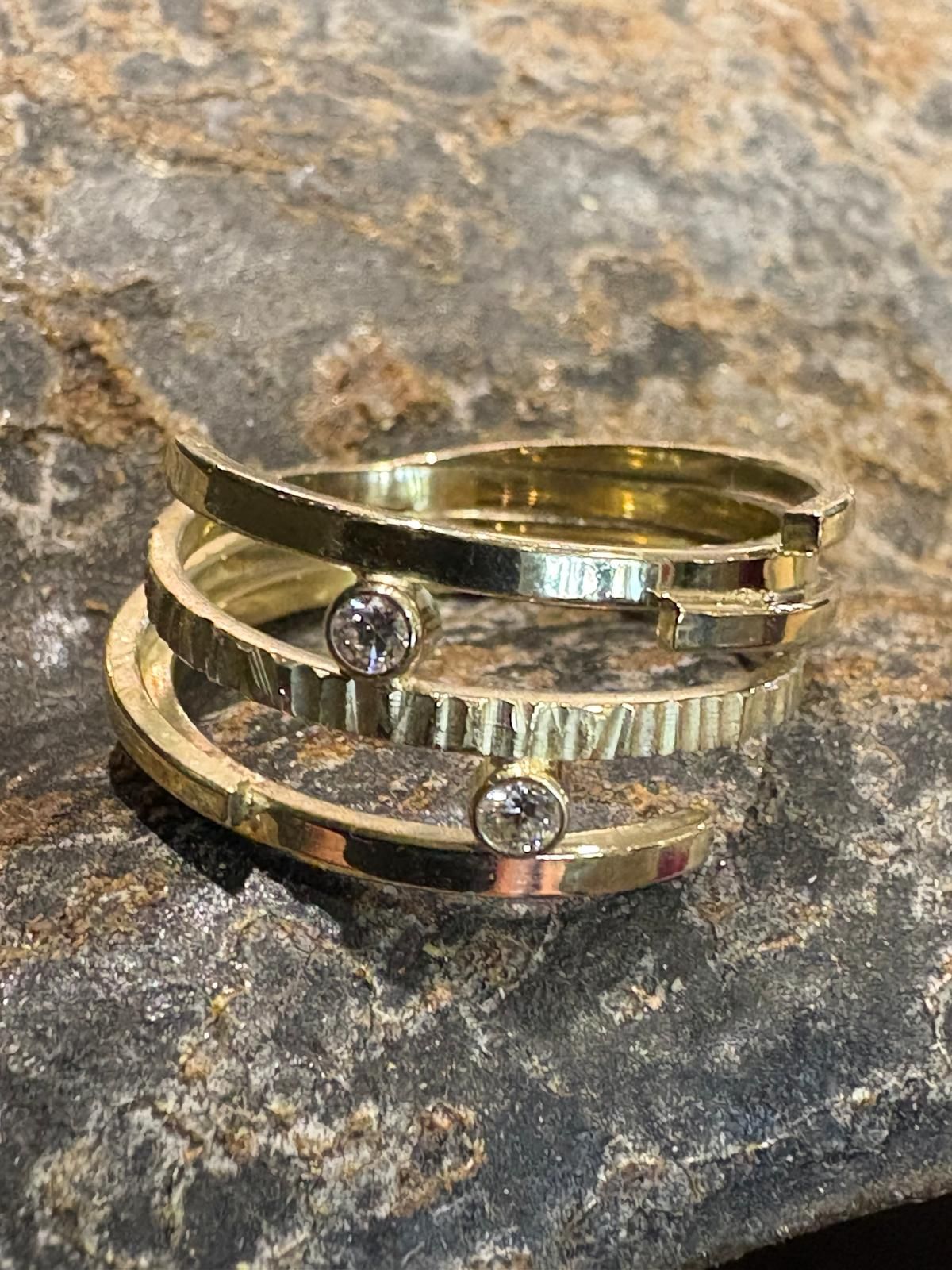 Gouden ring met drie overlappende banden, glad en gestructureerd, met twee kleine diamanten.