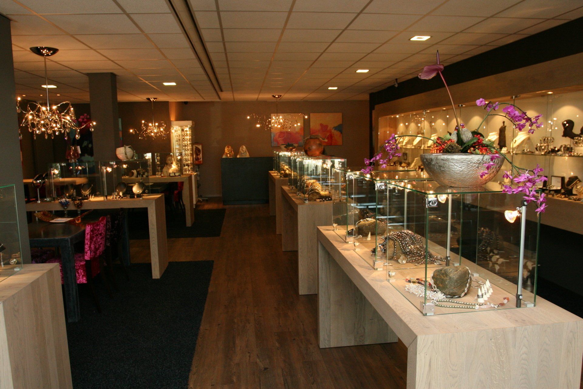 Interieur van een juwelierszaak met vitrines, houten vloer en diverse sieraden.
