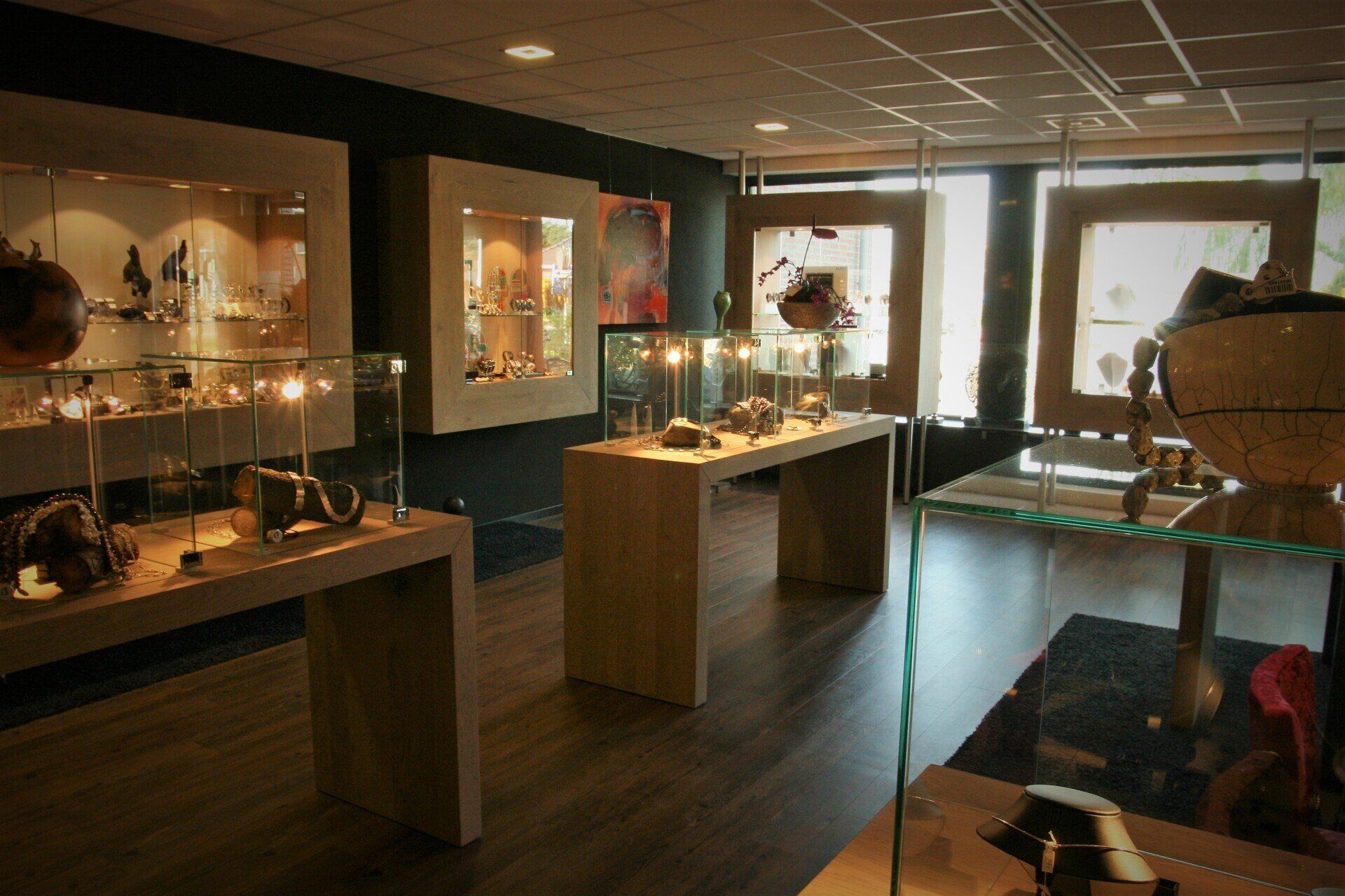 Interieur van een juwelierszaak met vitrines, houten accenten en kunstwerken op een donkere muur.
