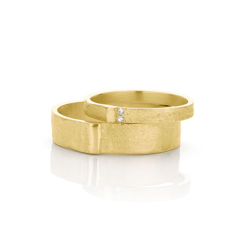 Twee getextureerde gouden trouwringen, waarvan één met twee kleine diamanten, op een witte achtergrond.