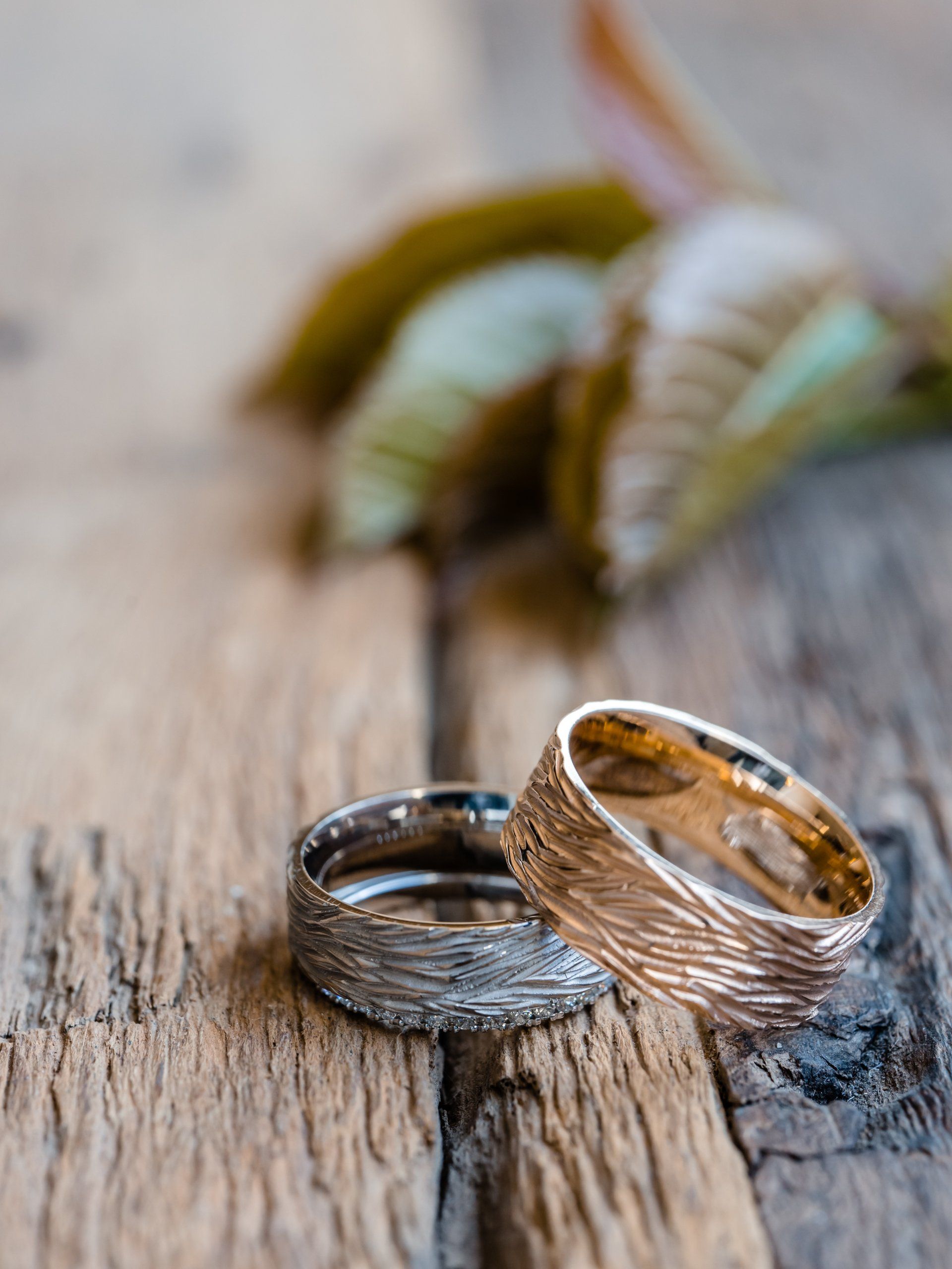 Twee gestructureerde trouwringen, zilver en goud, rusten op een rustiek houten oppervlak.