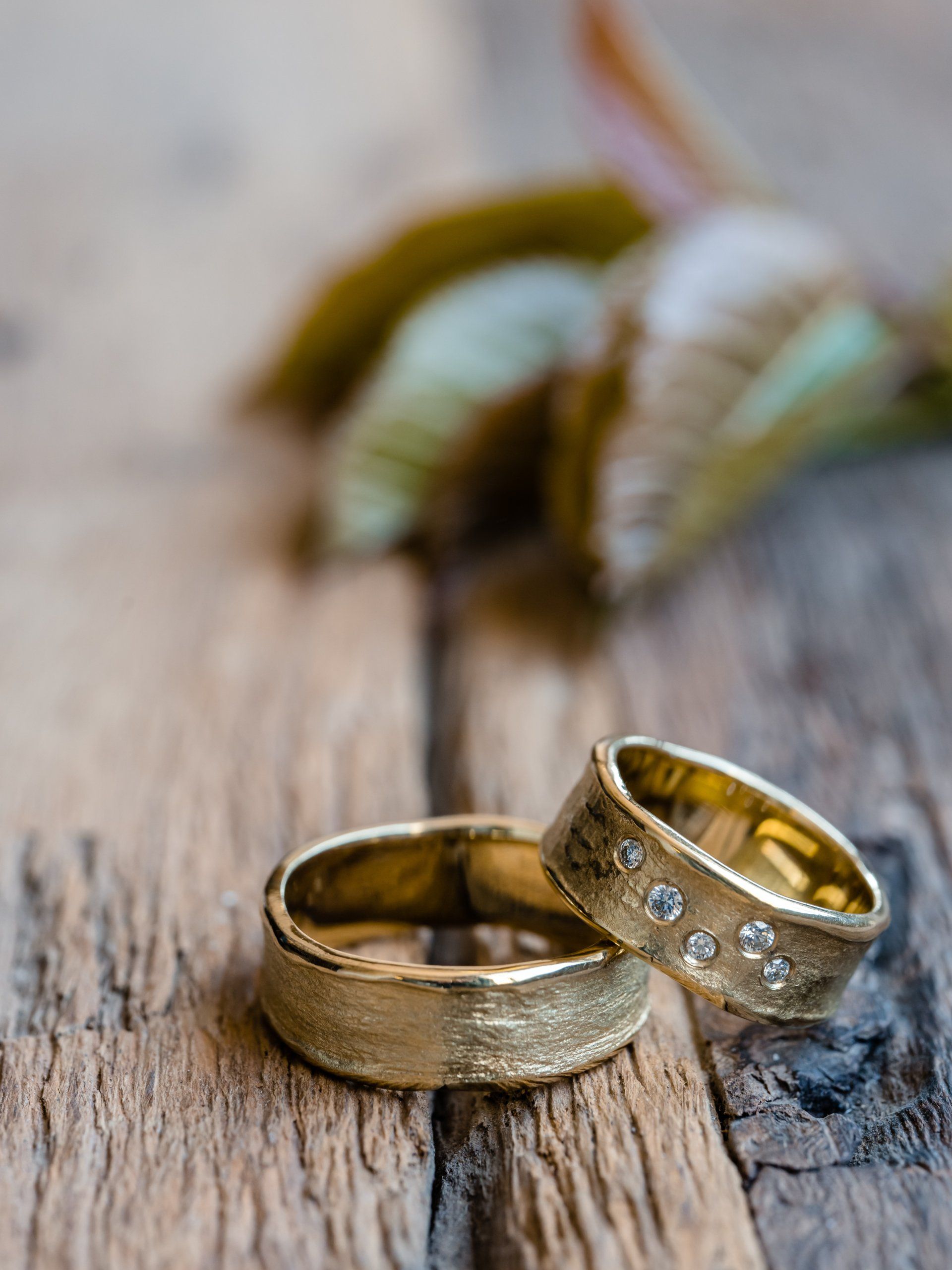 Twee gouden trouwringen op een verweerd houten oppervlak, met een plantenblad op de achtergrond.