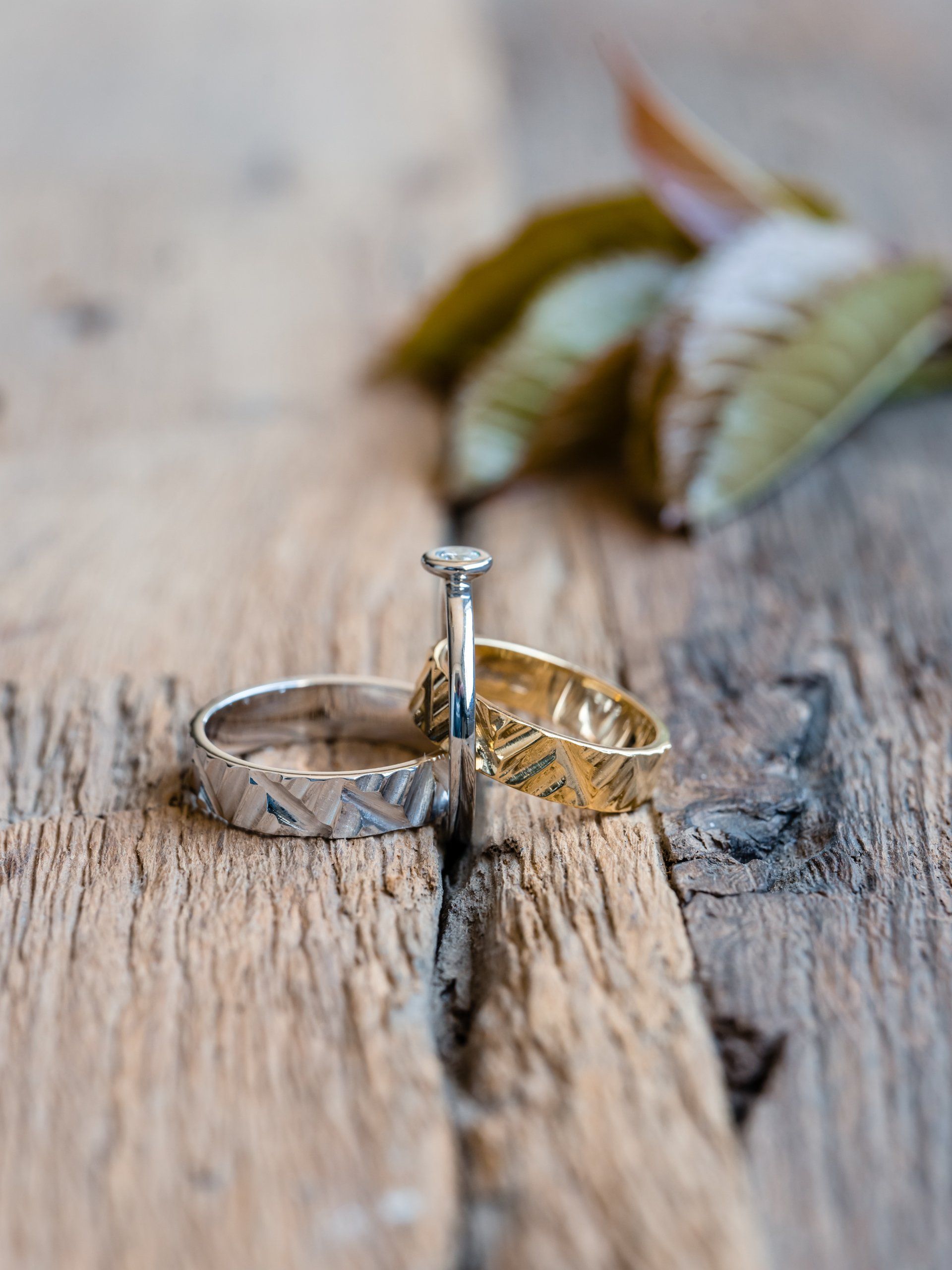 Trouwringen op rustiek hout, een zilveren band, een gouden band en een diamanten verlovingsring.