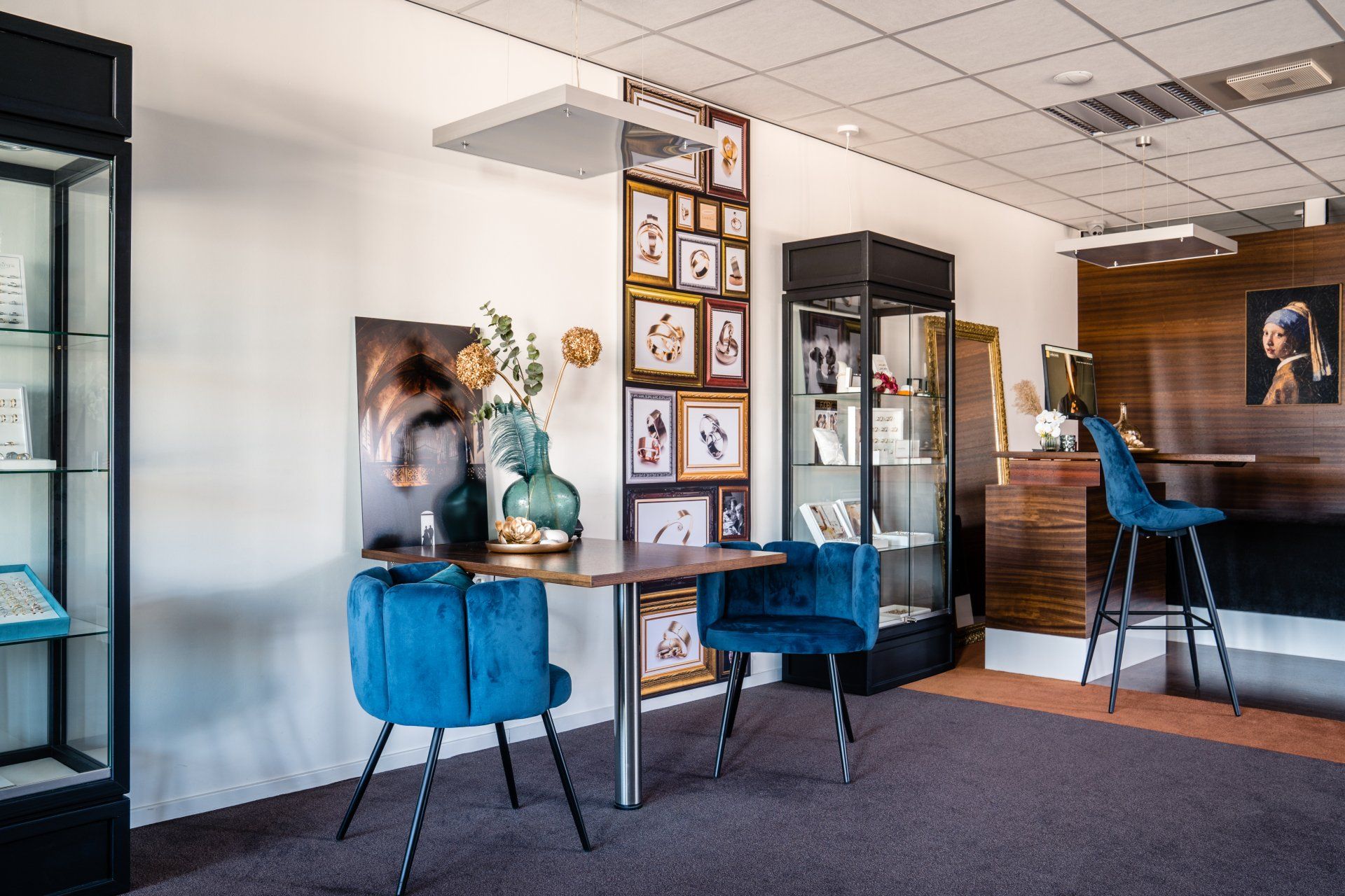Interieur van een kantoor met blauwe stoelen, kunstwerken, vitrinekasten en een houten accentmuur.