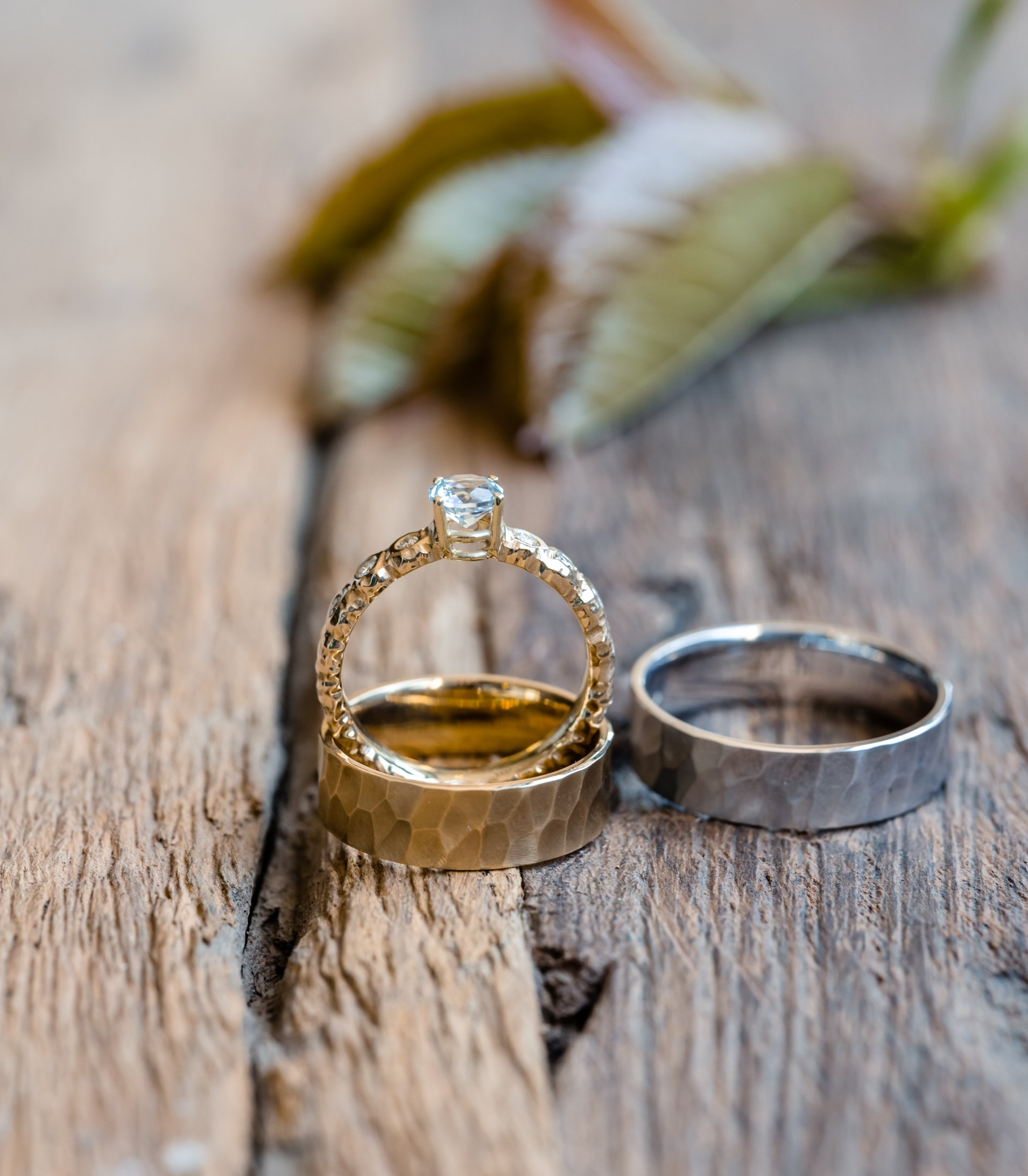 Trouwringen op een rustiek houten oppervlak; gouden band, diamanten ring, zilveren band en wazige bladeren.