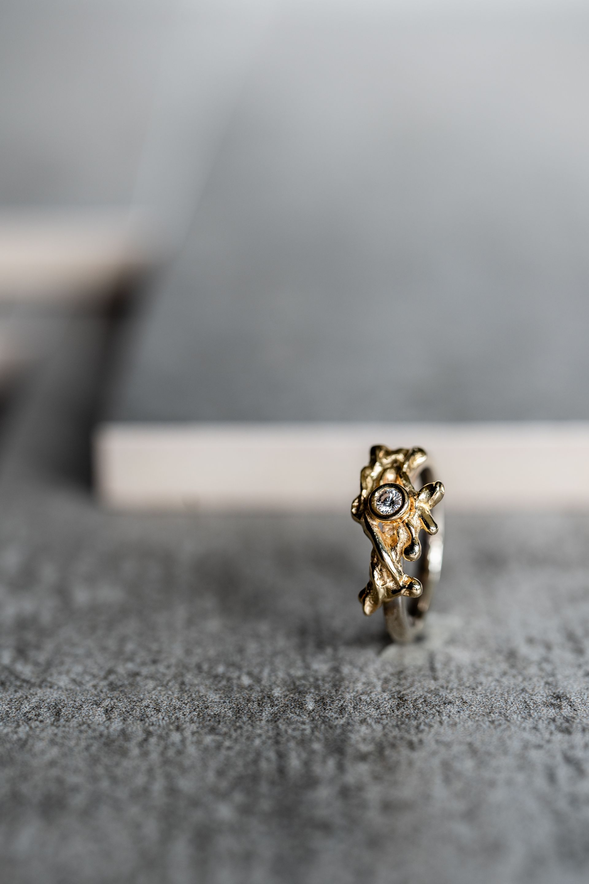 Gouden en zilveren ring met structuurontwerp en kleine edelstenen op een grijze ondergrond.