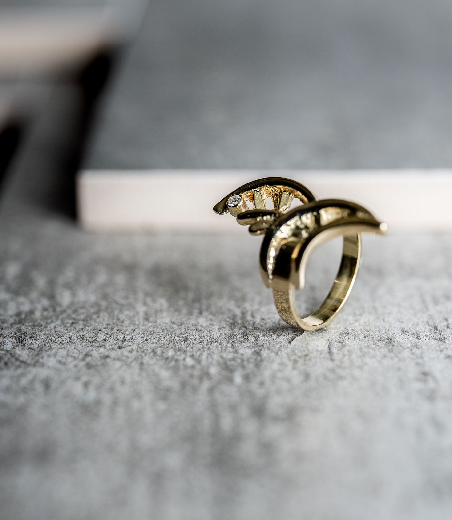 Goudkleurige ring met gebogen design op een grijs oppervlak, mogelijk beton.