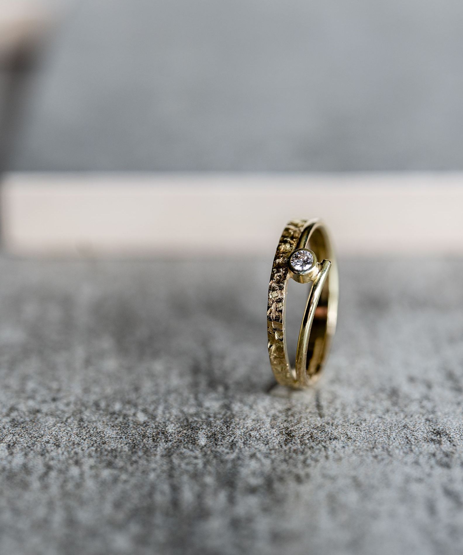 Gouden ring met een diamant in het midden op een grijs getextureerd oppervlak.