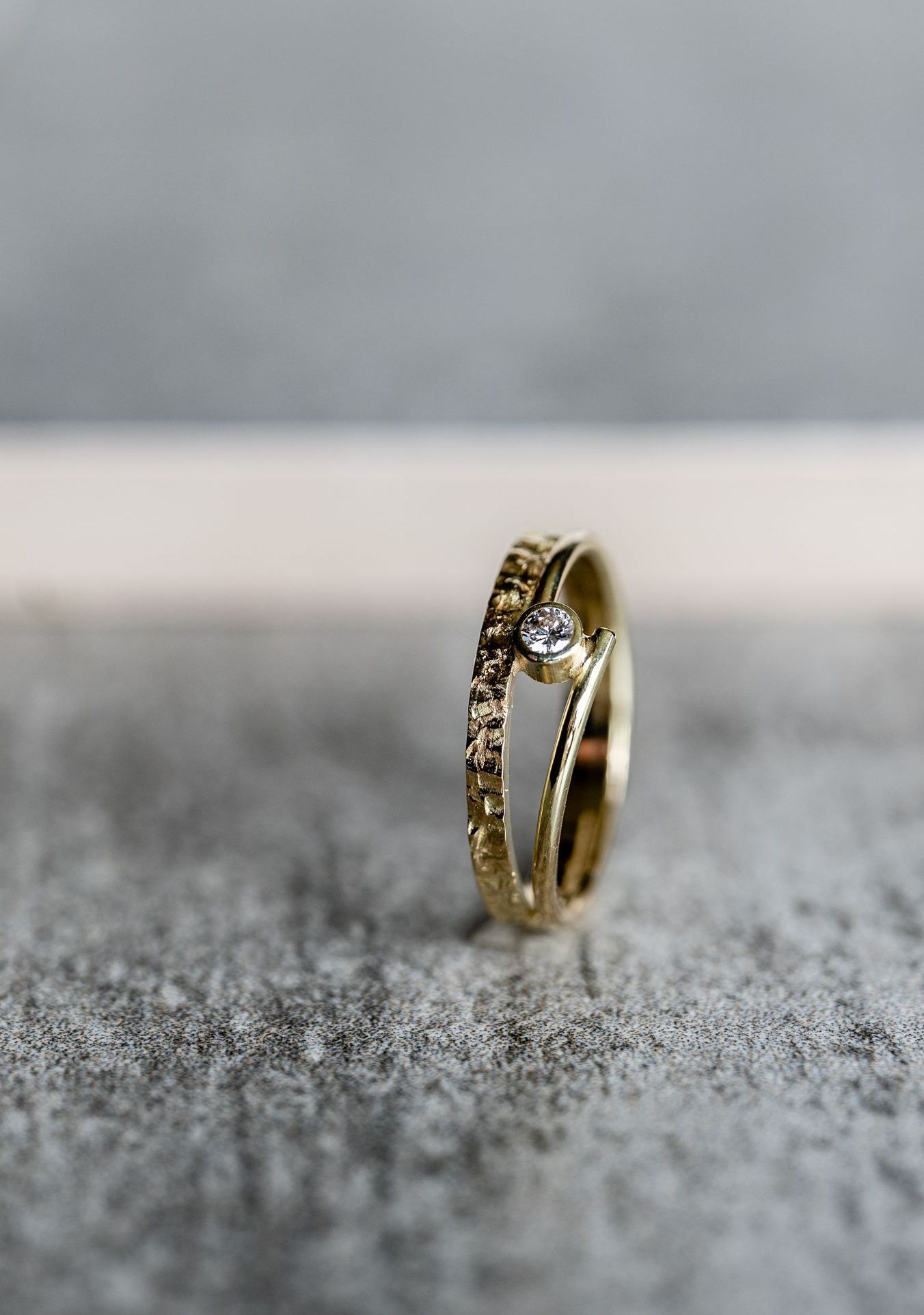 Gouden ring met een klein diamantje, op een grijs getextureerd oppervlak.