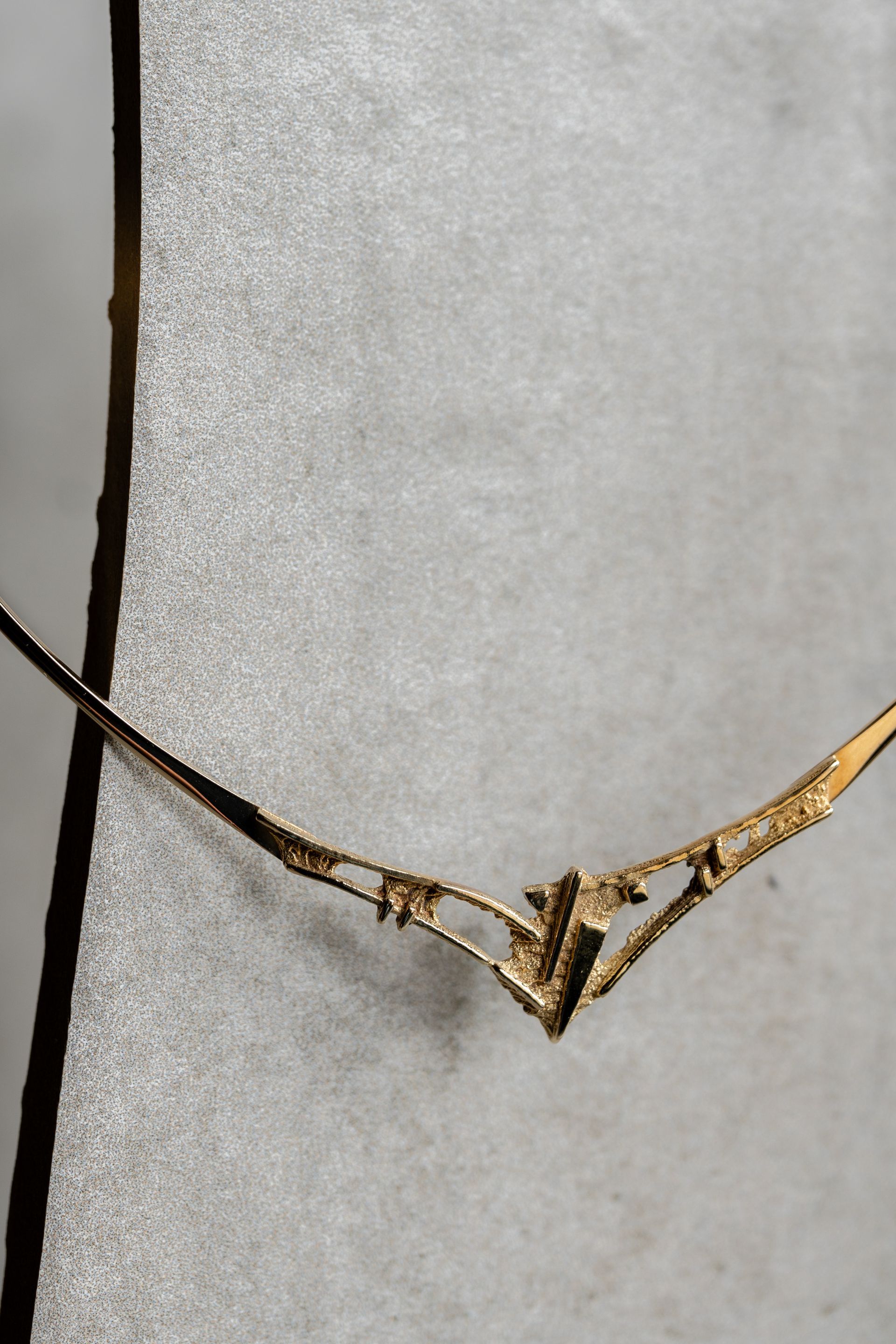 Gouden ketting op een grijze ondergrond; de hanger heeft een abstracte geometrische vorm.
