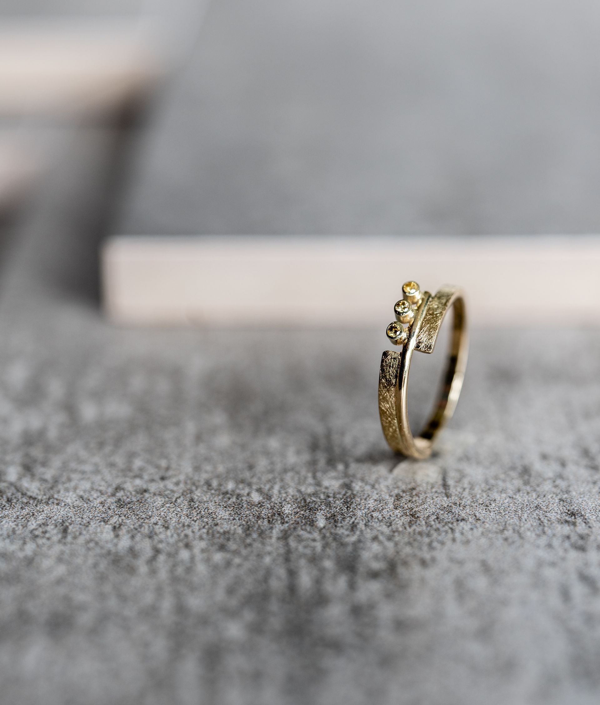 Gouden ring met kleine edelstenen op een grijs getextureerd oppervlak.