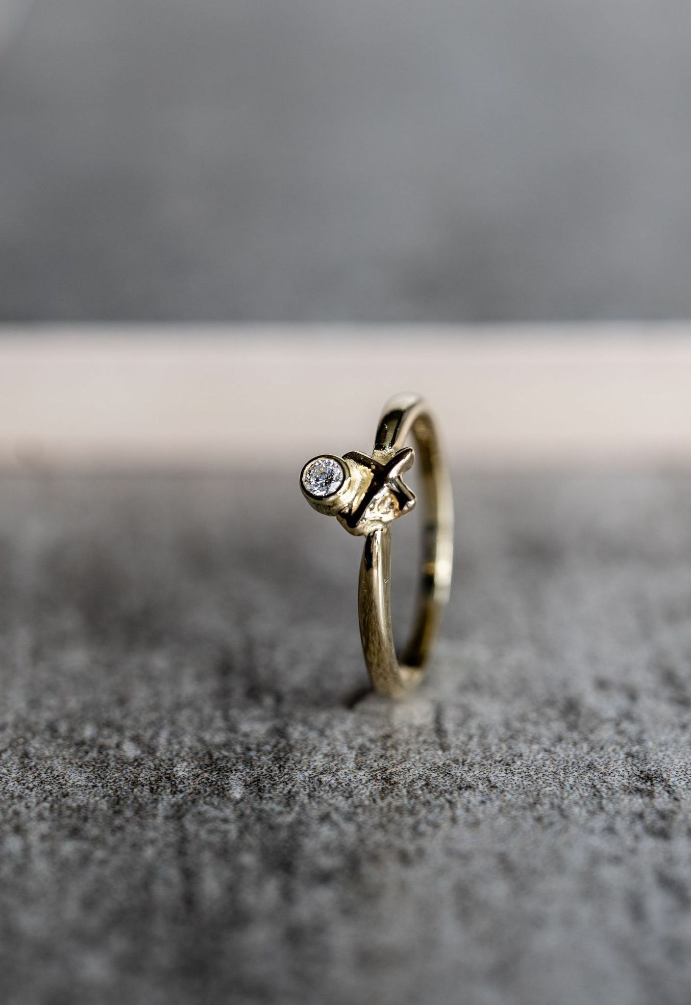 Gouden ring met een klein, helder steentje op een grijs getextureerd oppervlak.