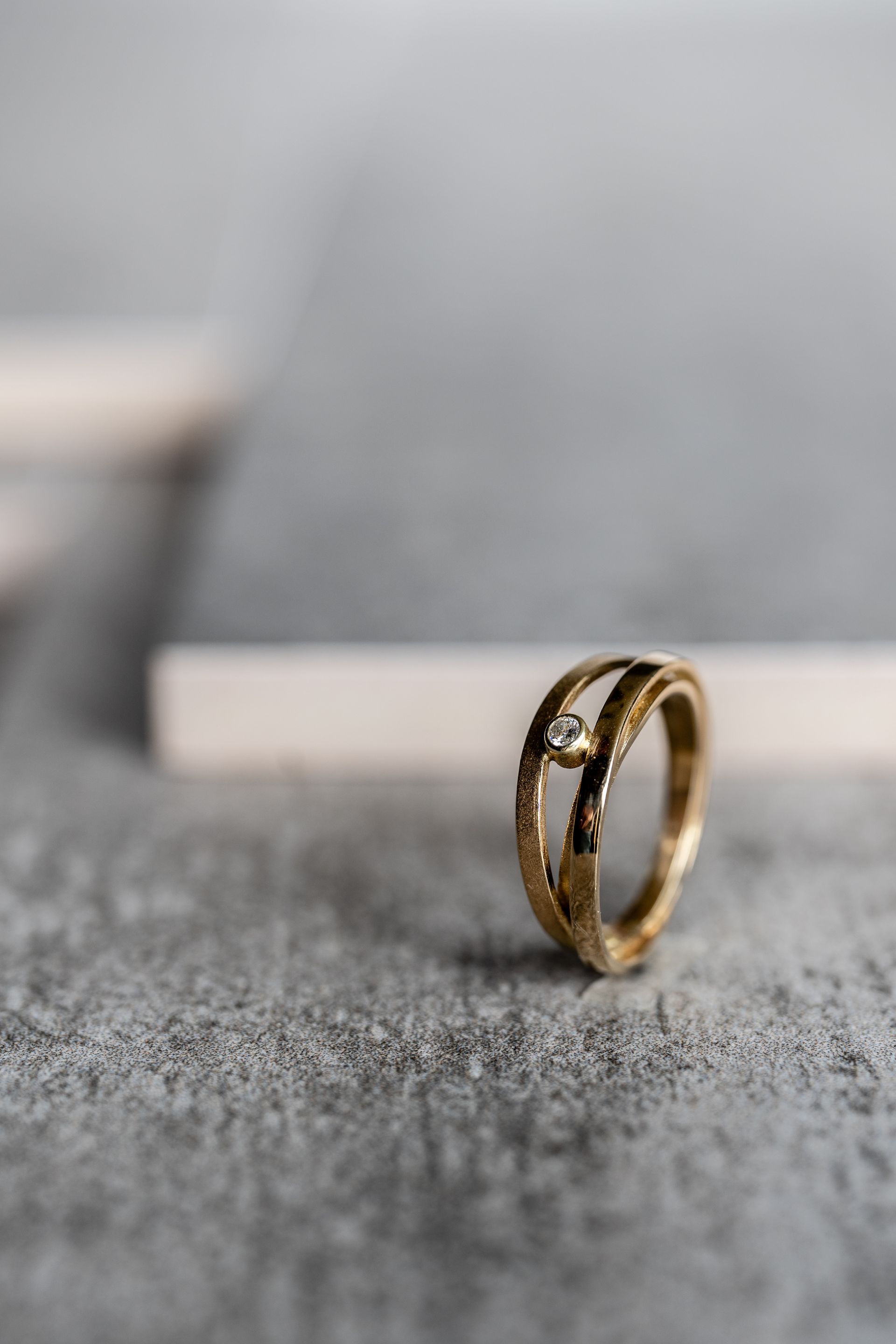 Gouden ring met een klein diamantje, op een grijze ondergrond met een onscherpe achtergrond.