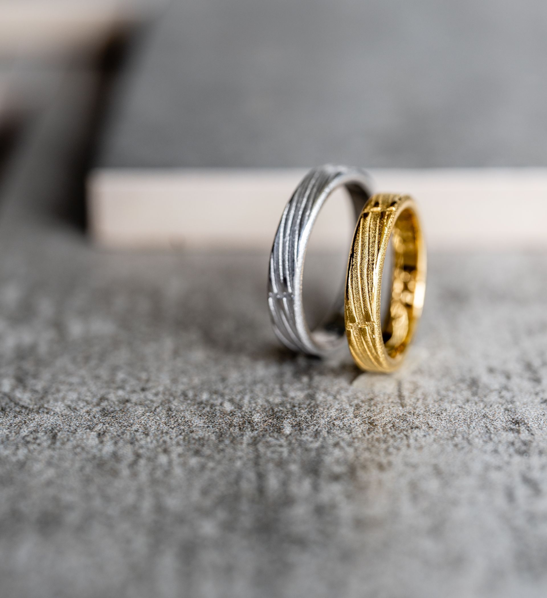 Twee getextureerde ringen: zilver en goud, op een grijs oppervlak.