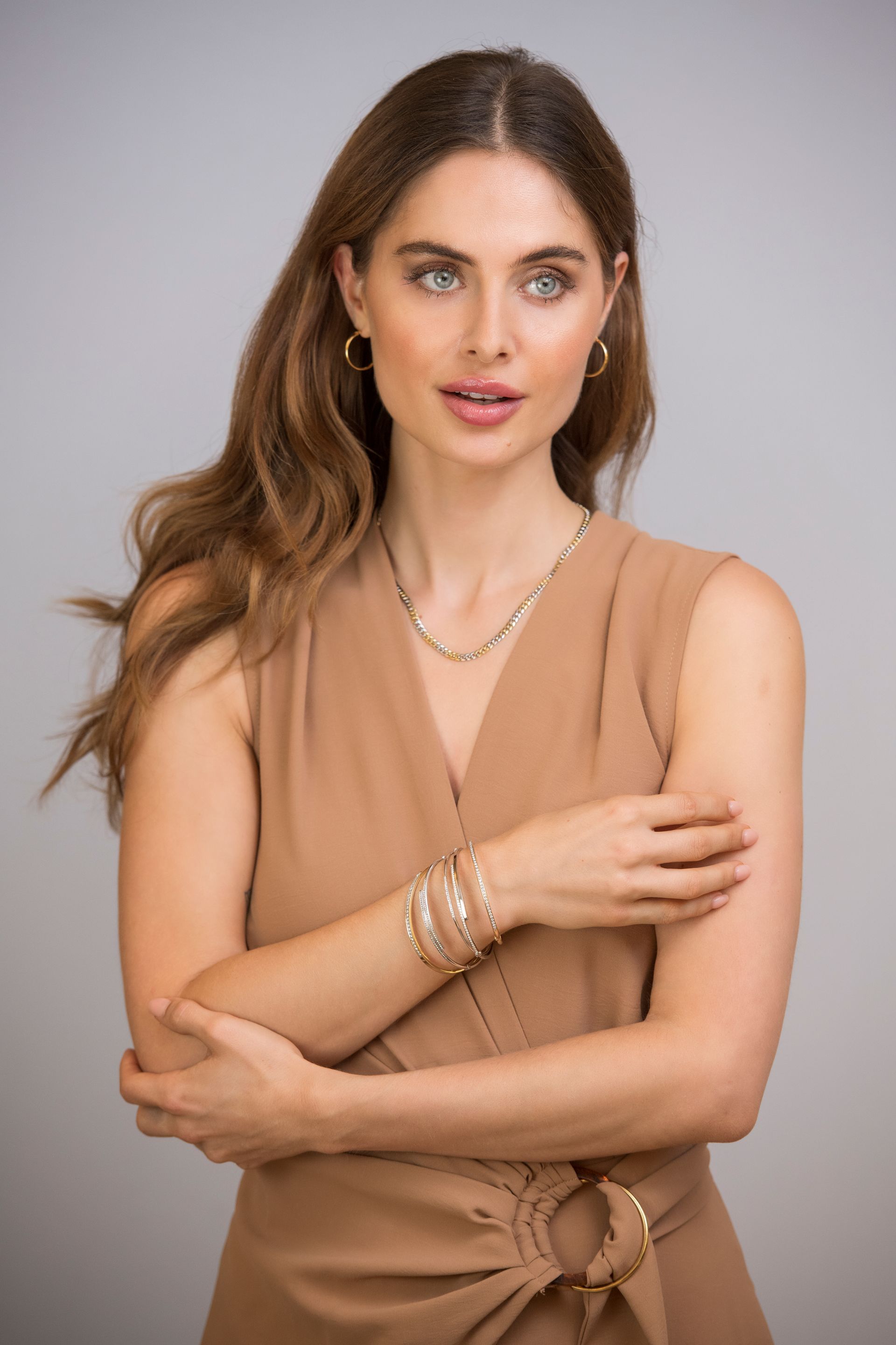 Vrouw in bruine jurk, met sieraden, kijkt iets opzij.