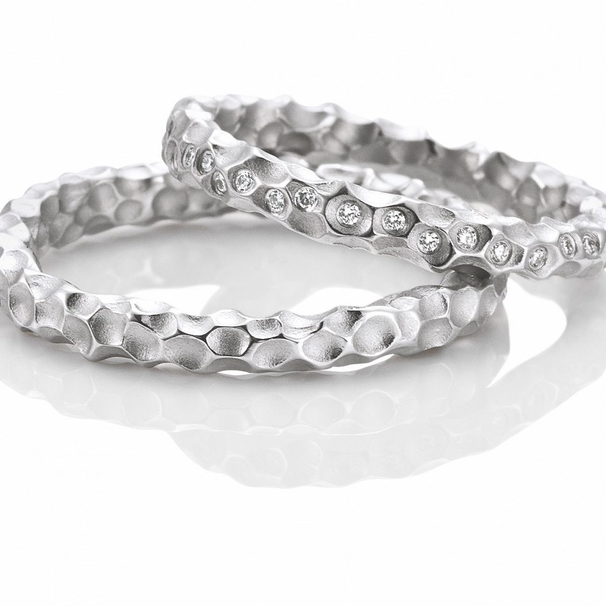 Twee zilveren ringen met structuur, waarvan één met ingelegde diamanten, op een wit oppervlak.
