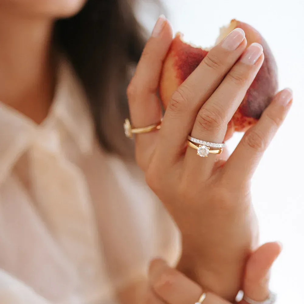 Een vrouw houdt in haar hand een perzik vast waar al een hap uit is genomen. Ze draagt meerdere ringen.