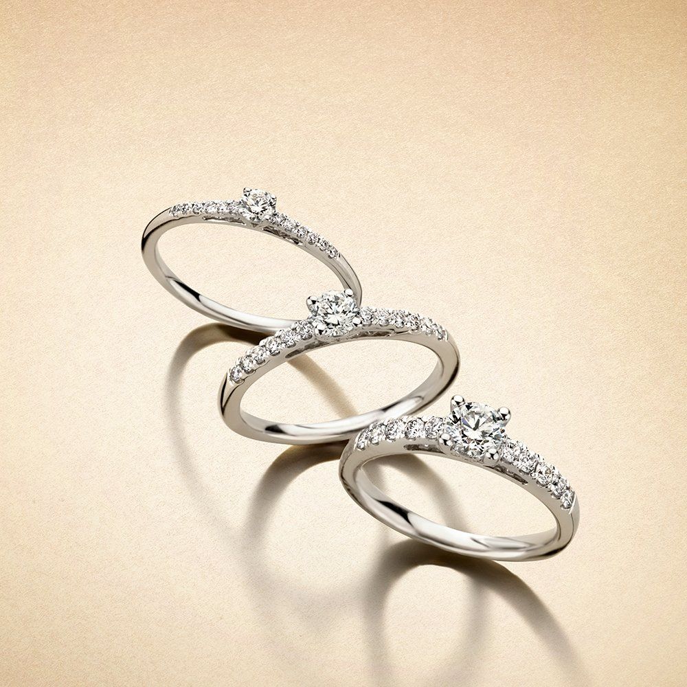 Drie diamanten ringen op een gouden oppervlak, elk met een centrale edelsteen en omliggende kleine steentjes.