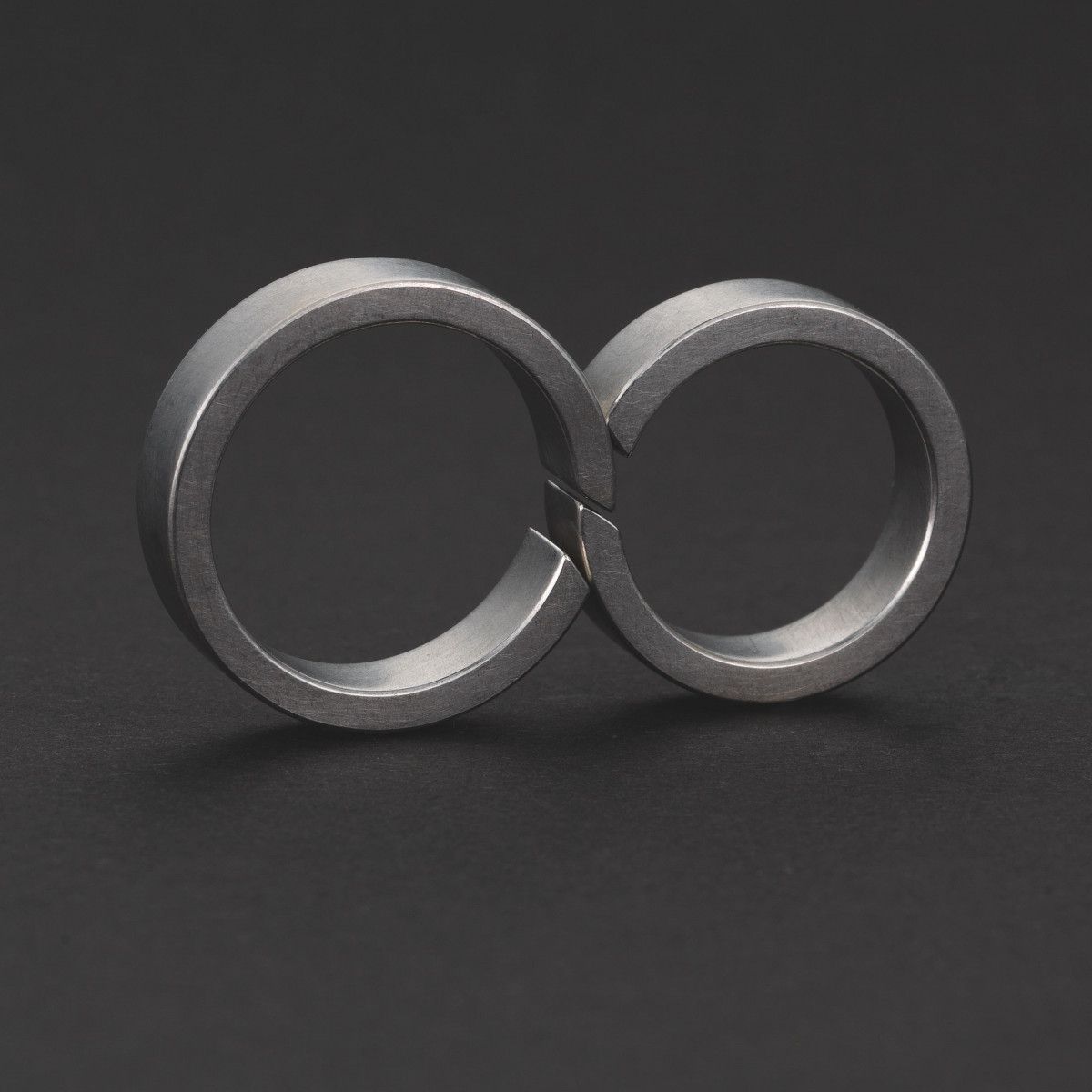Metalen ring in de vorm van een oneindigheidssymbool, liggend op een donkere ondergrond.