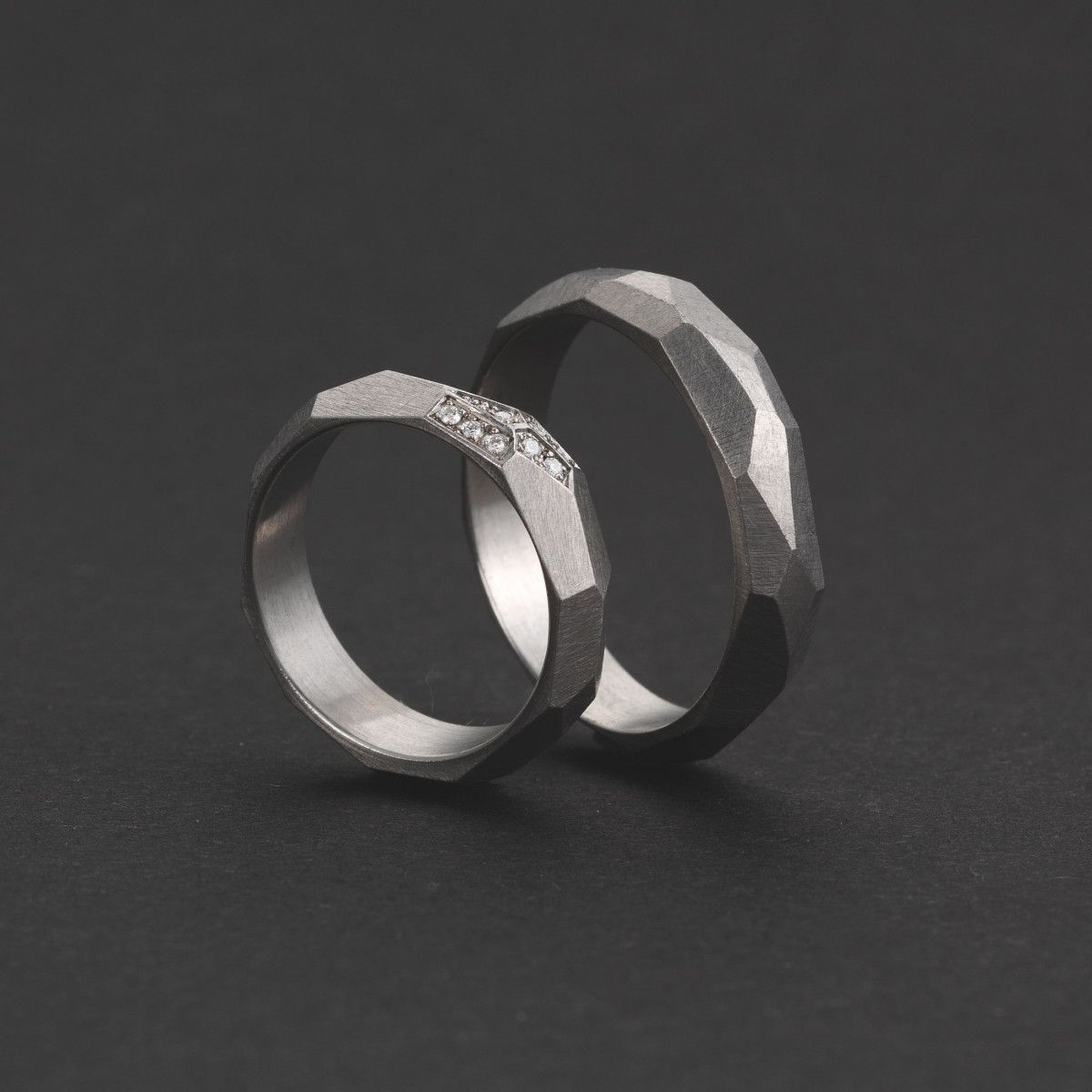 Twee zilveren trouwringen met gefacetteerde buitenkant, waarvan één met kleine diamanten.