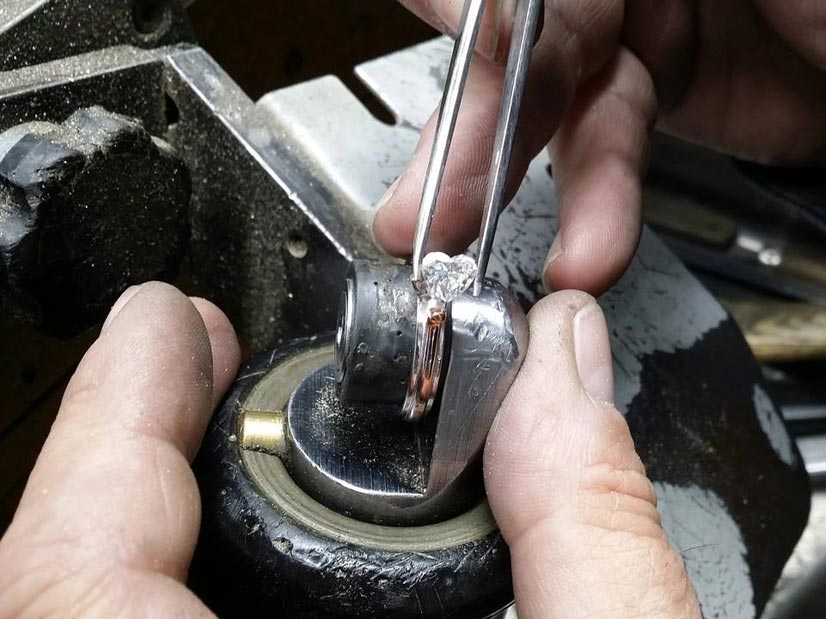 Close-up van handen die een pincet gebruiken om een ​​edelsteen in een sieradengereedschap te plaatsen.