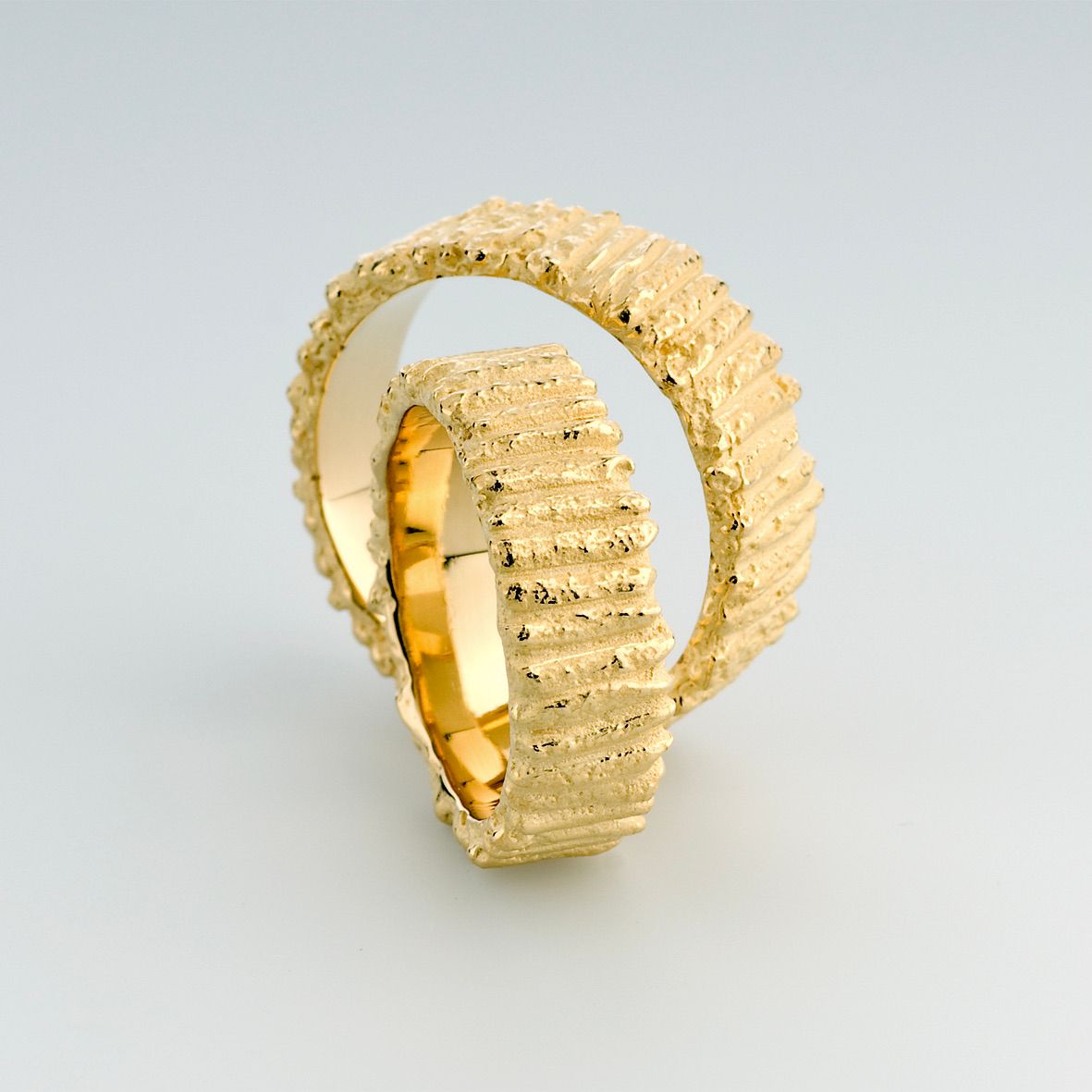 Twee getextureerde gouden ringen, de een in de ander, op een witte achtergrond.