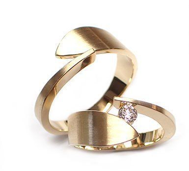 Twee gouden ringen met een modern, gebogen design, waarvan één met een klein diamantje.