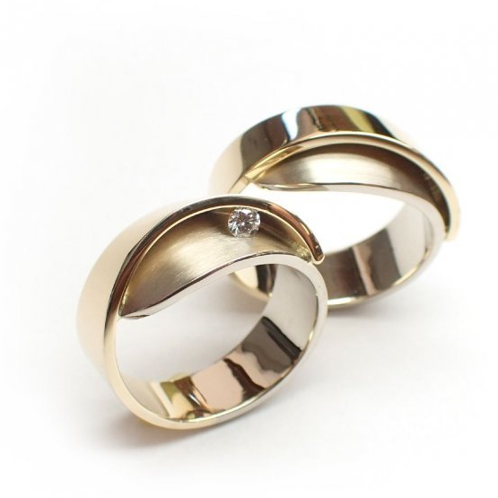 Twee gouden trouwringen, waarvan één met een klein diamantje, op een witte achtergrond.
