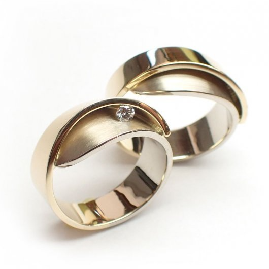 Twee gouden trouwringen, waarvan één met een klein diamantje, tegen een witte achtergrond.