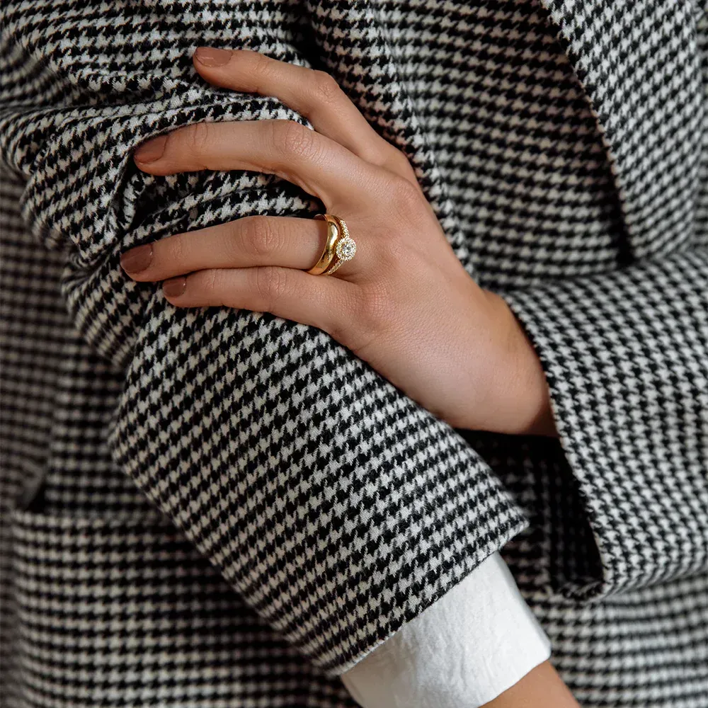 Hand met ring rustend op pied-de-poulemouw van blazer.