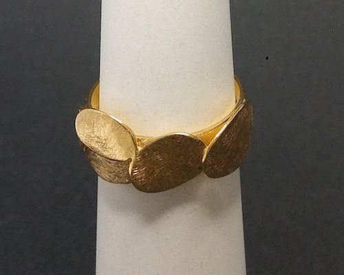Gouden ring met vier overlappende, ovale vormen met textuur op een witte standaard.