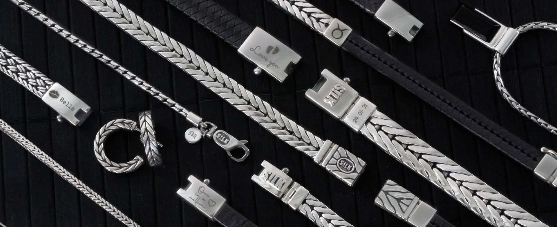 Close-up van zilveren armbanden en kettingen, verschillende stijlen, gerangschikt op een donkere ondergrond.